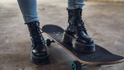 Close up view of a pair of legs wearing black leather boots with one foot on a black skateboard — Stock Photo