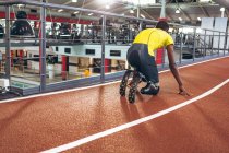 Vue arrière d'un athlète afro-américain handicapé en position de départ sur piste de course dans un centre de remise en forme — Photo de stock