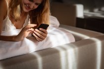 Nahaufnahme einer jungen kaukasischen Blondine, die mit dem Smartphone im Bett liegt. — Stockfoto