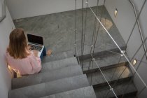 Підвищений задній вигляд молодої кавказької жінки, що носить рожеву сорочку, сидячи на сходових сходах за допомогою портативного комп'ютера. — стокове фото