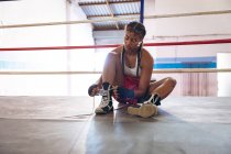 Front view of female boxer tying shoelaces in boxing ring at fitness center. Strong female fighter in boxing gym training hard. — Stock Photo