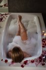 Возвышенный вид молодой женщины, лежащей в пенной ванне с зажженными свечами и лепестками роз вокруг . — стоковое фото