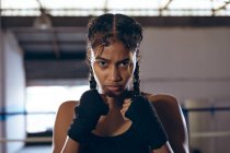 Mulher pugilista afro-americana com punho a olhar para a câmara no clube de boxe. Forte lutador feminino no treinamento de ginásio de boxe duro . — Fotografia de Stock