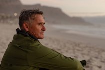 Side view close up of a mature Caucasian man enjoying the view sitting on a beach beside the sea at sunset — Stock Photo