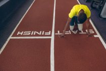 Vista ad alto angolo di disabile afroamericano atletico maschile al punto di partenza sulla pista da corsa nel centro fitness — Foto stock