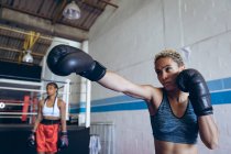 Вид спереди женщины-боксера, практикующей бокс в боксерском клубе. Сильная женщина-боец в боксёрском зале тяжело тренируется
. — стоковое фото
