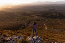 Back view of a young woman standing on a rock with her arms outstretched, enjoying the view during a stop off on a road trip. — Stock Photo
