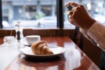 Side view close up of the hands of man taking photos of his croissant with a smartphone, sitting at a table inside a cafe. Digital Nomad on the go. — Stock Photo