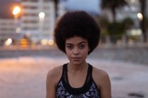 Ritratto da vicino di una giovane donna di razza mista che indossa abiti sportivi guardando dritto alla telecamera all'esterno in uno spazio urbano al crepuscolo — Foto stock
