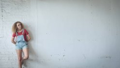 Vista frontale di una giovane donna caucasica con i capelli ricci in piedi contro un muro bianco — Foto stock