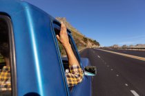 Rear view of man with his arm leaning out of the side window of a pick-up truck, holding the roof as he drives down the highway on a road trip — Stock Photo