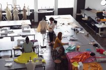 Blick aus der Vogelperspektive auf eine vielfältige Gruppe von Modestudenten, die in einem Atelier der Modehochschule an Entwürfen arbeiten — Stockfoto