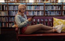 Vista lateral de cerca de una joven estudiante asiática usando un hijab usando una tableta y estudiando en una biblioteca - foto de stock
