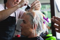 Вид сбоку на белого парикмахера средних лет и молодую белую женщину с раскрашенными волосами в парикмахерской — стоковое фото