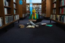 Vista frontale di una giovane studentessa asiatica che indossa un hijab con in mano un libro, usa un computer portatile e studia in una biblioteca — Foto stock