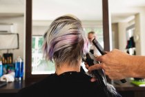 Vue arrière rapprochée d'un coiffeur caucasien d'âge moyen et d'une jeune femme caucasienne se faisant couper les cheveux dans un salon de coiffure, reflétée dans un miroir — Photo de stock