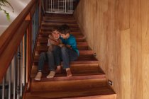 Porträt von zwei kaukasischen Jungen, die zu Hause auf einer Treppe sitzen, sich umarmen und in die Kamera schauen — Stockfoto