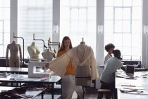 Vista frontale di una giovane studentessa caucasica che lavora su un indumento su un manichino in uno studio del fashion college, con altri studenti che lavorano sullo sfondo — Foto stock