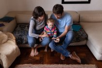 Передній вигляд молодого кавказького батька і матері, які сидять на дивані і користуються смартфоном зі своїм немовлям. — стокове фото