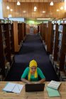 Vorderseite einer jungen asiatischen Studentin, die einen Hijab trägt, einen Laptop benutzt und in einer Bibliothek studiert — Stockfoto