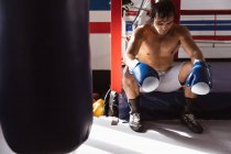 Vista frontal de cerca de un joven boxeador masculino de raza mixta sentado en un ring de boxeo - foto de stock