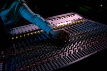 Visão frontal seção média do engenheiro de som masculino chegando através de uma mesa de mistura em um estúdio de gravação para ajustar uma configuração de canal — Fotografia de Stock