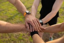 High angle low section of three adults standing together and stacking their hands in unity at an outdoor gym during a bootcamp training session — Stock Photo