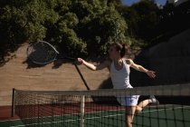 Seitenansicht einer jungen kaukasischen Frau, die an einem sonnigen Tag Tennis spielt und rennt, um einen Ball mit einer Wand hinter sich zu schlagen — Stockfoto