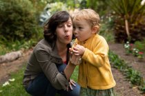Front view close up of a young Caucasian mother blowing a dandelion with her baby in a garden — Stock Photo