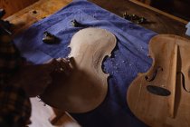 Крупный план женщины-лютистки, работающей над телом скрипки на верстаке в своей мастерской — стоковое фото