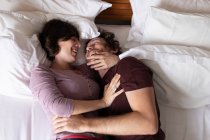 Бічний вид на молодого кавказького чоловіка і жінку лежить у ліжку, посміхаючись і обіймаючи — стокове фото