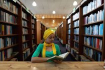 Вид спереди на молодую азиатскую студентку в хиджабе, читающую книгу и занимающуюся в библиотеке — стоковое фото