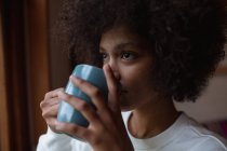 Крупним планом портрет молодої змішаної раси жінки, яка дивиться, як п'є чашку кави — стокове фото