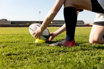 Side view low section of female rugby player kneeling on a rugby pitch and setting the ball on a tee for a place kick — Stock Photo