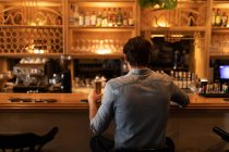 Vista trasera de un joven caucásico relajándose de vacaciones en un bar, bebiendo cerveza - foto de stock