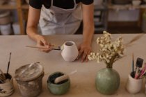 Vista elevata di una donna che si appoggia su un tavolo da lavoro e invecchia una pentola in uno studio di ceramica, con pentole e utensili in primo piano — Foto stock
