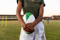 Передня частина жіночого регбіста, що стоїть на спортивному полі, тримає м'яч регбі під час тренувальної сесії — стокове фото