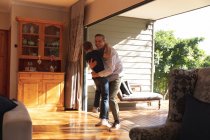Vista frontal de um homem caucasiano de meia-idade abraçando com seu filho pré-adolescente depois de chegar em casa — Fotografia de Stock