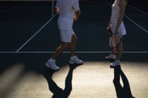 Vue latérale de la femme et d'un homme jouant au tennis par une journée ensoleillée, se faisant face et parlant — Photo de stock