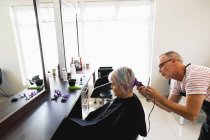Вид сбоку на белого парикмахера средних лет и молодую белую женщину с подстриженными волосами в парикмахерской — стоковое фото