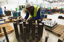Vista frontal close-up de um jovem trabalhador de fábrica afro-americano preparando uma peça de máquina em um armazém em uma fábrica de processamento — Fotografia de Stock