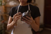 Вид спереди на молодую кавказскую гончарку с глиняной фляжкой и модельным инструментом в керамической мастерской — стоковое фото
