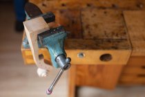 Close up of a vice with the scroll of a violin attached to a workbench in a workshop — Stock Photo
