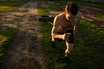 Vue de face d'un jeune homme caucasien torse nu tirant un pneu sur une corde autour de sa taille dans une salle de gym extérieure lors d'une séance d'entraînement bootcamp — Photo de stock