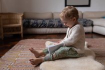 Vista laterale di un bambino caucasico seduto su un pavimento e con in mano un taccuino, a piedi nudi — Foto stock