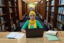 Retrato de uma jovem estudante asiática vestindo um hijab usando um computador portátil e estudando em uma biblioteca — Fotografia de Stock