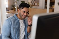 Вид спереди на молодого расиста, сидящего за столом в наушниках и смотрящего на экран компьютера в креативном офисе — стоковое фото