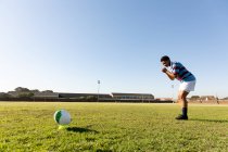 Vista lateral de uma jovem adulta de raça mista jogadora de rugby em pé em um campo de rugby se preparando para correr até a bola e fazer um chute no lugar — Fotografia de Stock