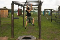 Rear view of a young Caucasian man hanging from monkey bars at an outdoor gym during a bootcamp training session, with other participants in the background — Stock Photo