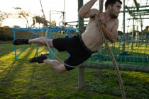 Front view of a young Caucasian woman man swinging on a rope through a hoop at an outdoor gym during a bootcamp training session — Stock Photo